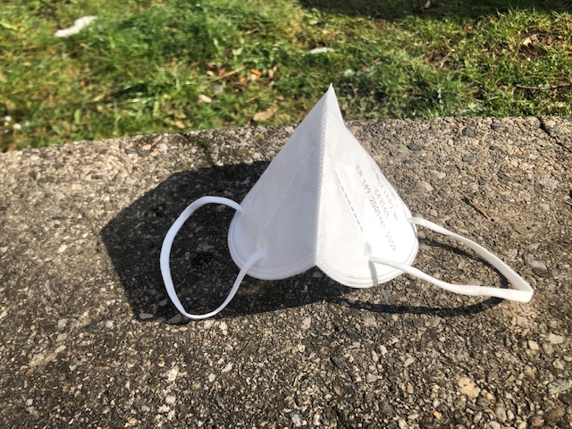 Eine weiße FFP2-Maske liegt am Boden in der Sonne